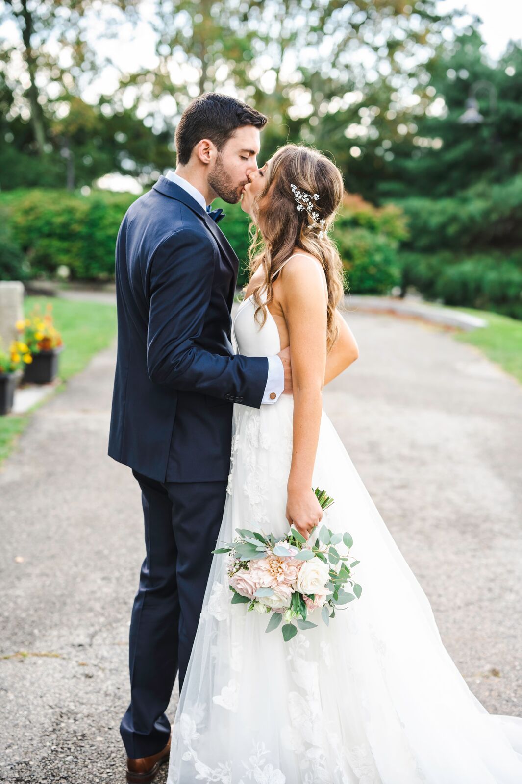 Couple kissing on a tree lined garden path, bouquet in hand