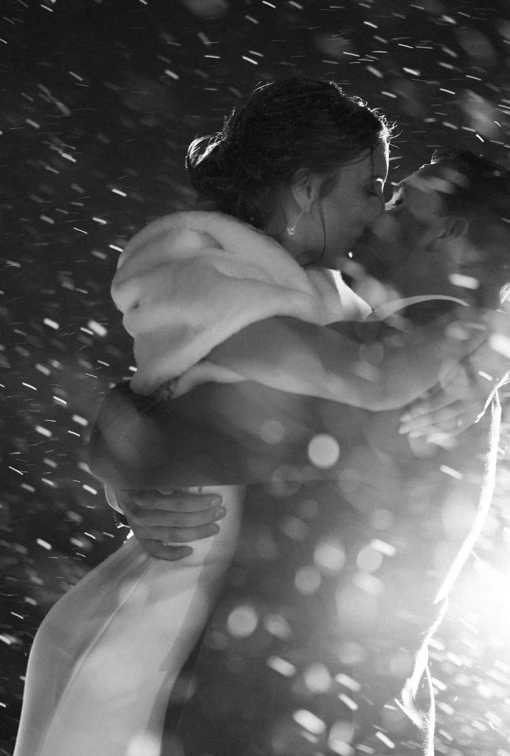 Bride and groom embracing at night as snow falls