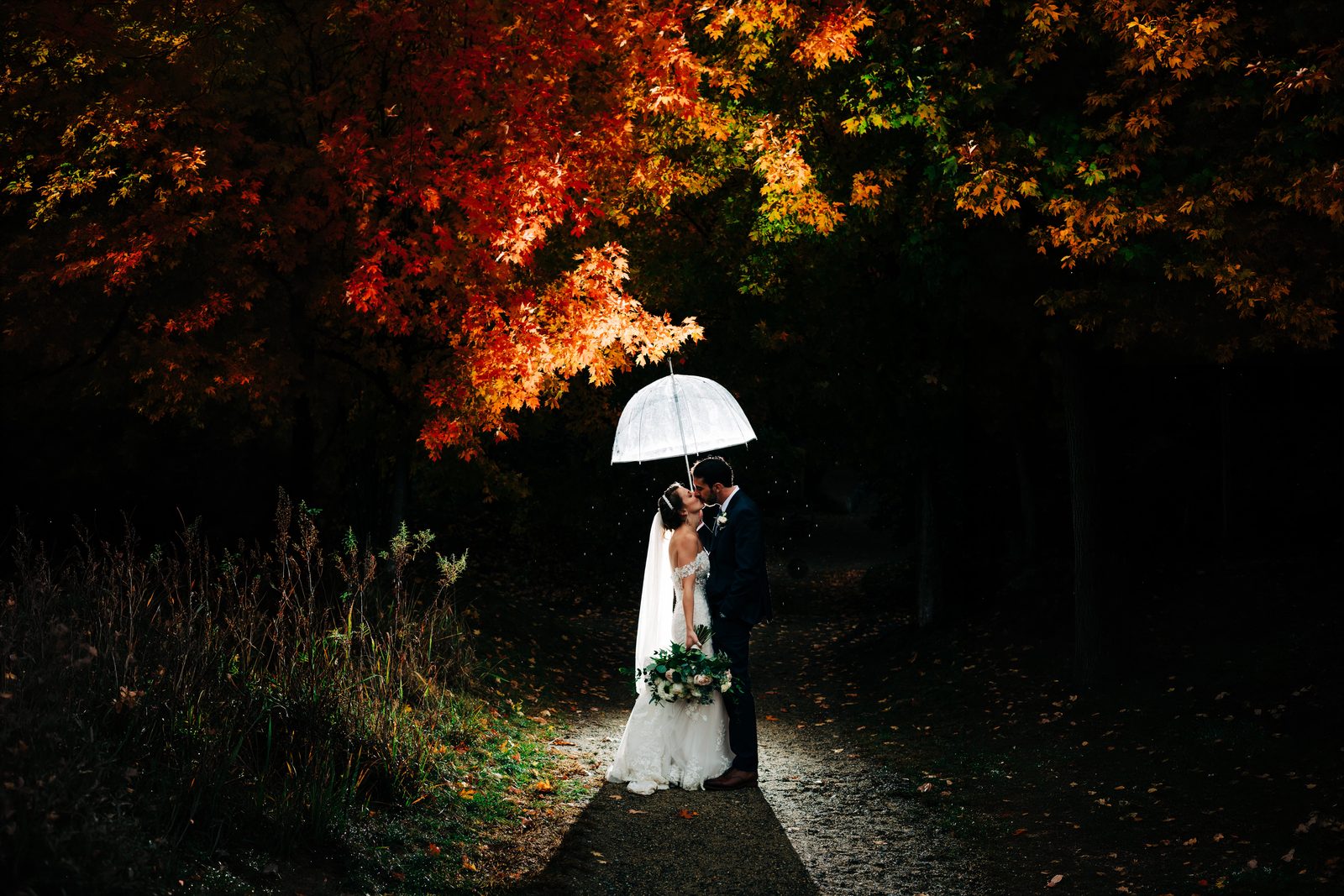 Bride and groom kissing under a clear umbrella among New Hampshire autumn foliage