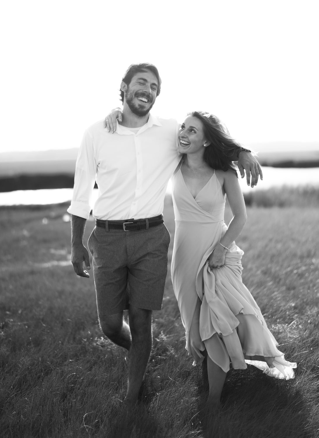 Bride and groom laughing while walking through a field in black and white
